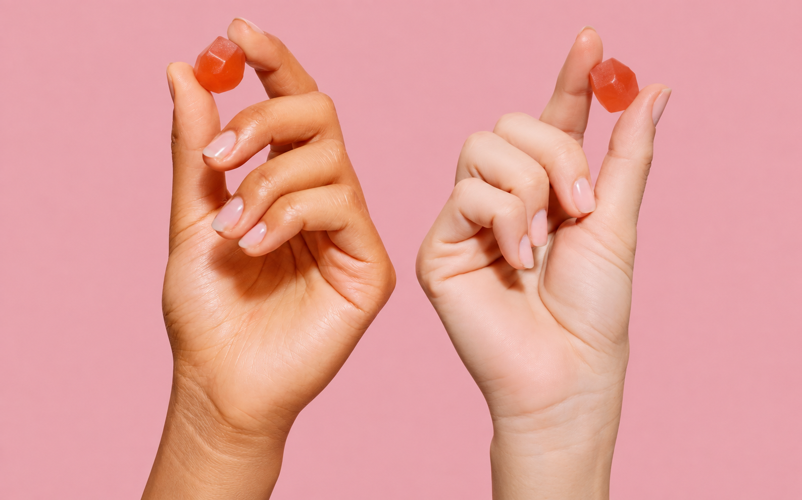 Two hands each holding a single gummy against a pink background